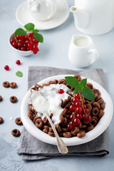 Healthy breakfast with chocolate corn rings, red currant berries, yogurt and tea on a gray concrete background. Selective focus. Top view. Copy space.