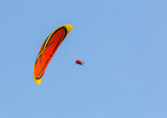 Orange and yellow paraglider on clear blue sky
