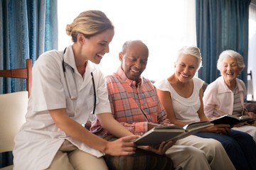 Smiling female doctor reading book to senior people sitting on