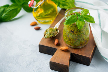 Homemade delicious green pesto in a glass jar. On a gray concrete background. Traditional Italian sauce. Selective focus.