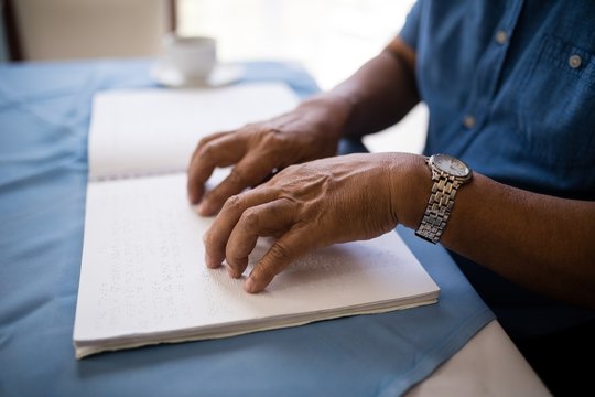 Midsection of senior man reading braille book at table