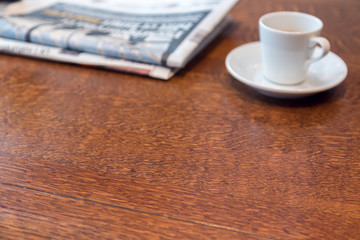 Top view of wood table. Espresso coffee cup and newspapers blurred background. Morning coffee concept.