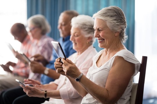 Row of smiling senior people sitting on chairs using digital