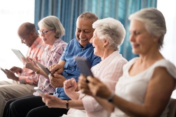 Smiling senior people sitting on chairs while using digital