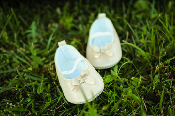 Cute beige pair of baby shoes on green grass