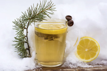 glass cup of tea with lemon slice wrapped in a knitted scarf on the snow