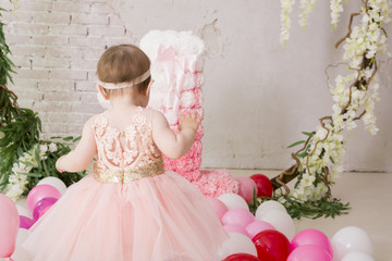 A little cheerful girl in a pink dress is beside the air balloons.