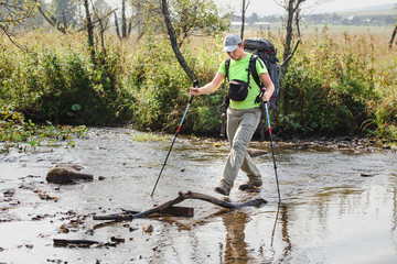 Backpacker trekker wading small mountain river, hiking concept