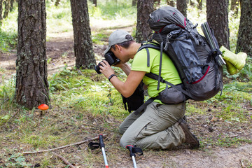 Photographer with camera making a photo of Amonita mushroom outdoors in the forest