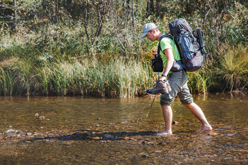 Backpacker trekker wading small mountain river, hiking concept