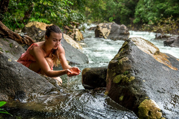 the girl drinks water from a mountain stream