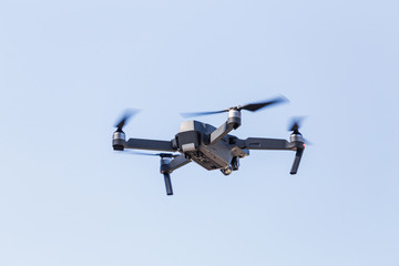 A beautiful modern black drone quadrocopter with the photo and a video camera on the board flies against the blue sky