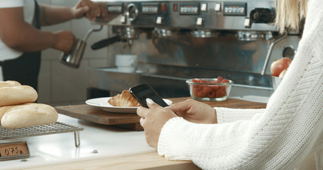 Attractive young woman wearing a white sweater in a loft style bakery or coffee shop with a smartphone