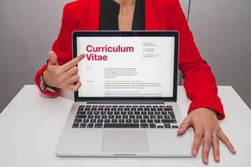 Woman showing curriculum vitae on laptop. Foreign text is latin. Text meaning: generic CV pre filled. All data showing a generic format for cv, without reference to someone or somewhere.