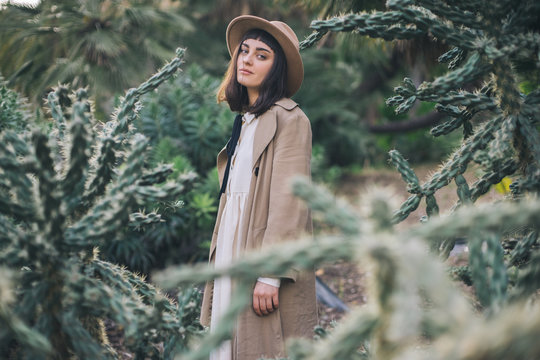 Dreamy brunette girl walks in cacti park wearing old fashioned white dress and brown hat