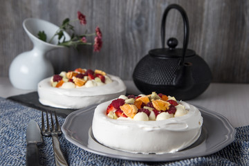 Perfect tea time, meringue dessert Pavlova cake with fresh berries and a teapot on a table.