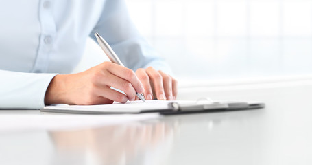 Woman's hands writing on sheet  in a clipboard with a pen, isolated on desk