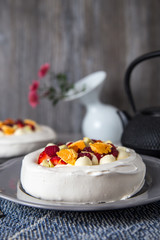 Perfect tea time, meringue dessert Pavlova cake with fresh berries and a teapot on a table.