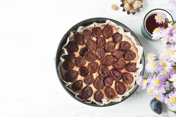Whole plum cake with tea mug, fresh plums, brown sugar and flowers. Top view.