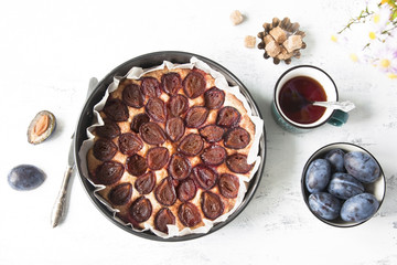 Whole plum cake with tea mug, fresh plums, brown sugar and flowers. Top view.
