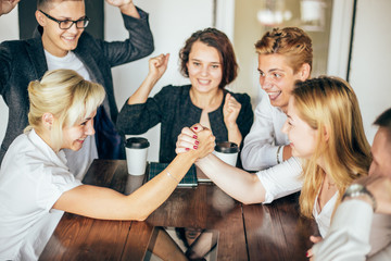 two businesswoman armwrestling at table, trying to get leadership