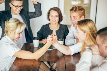 two businesswoman armwrestling at table, trying to get leadership - obrazy, fototapety, plakaty