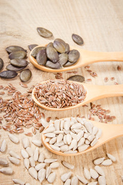 Flaxseed, pumpkin and sunflower seeds in wooden spoons.