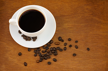Coffee in white cup and saucer and coffee beans on brown wooden background.