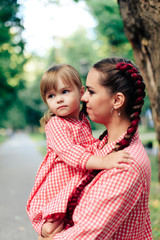 Obraz premium young happy family with little beautiful baby with blue eyes walking in summer park at sunset. Mom and little daughter in identical pink dresses