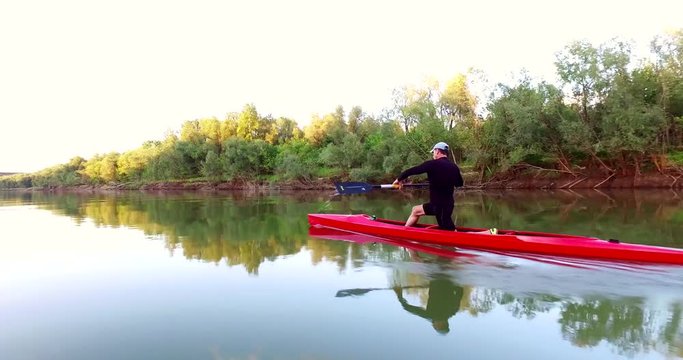 Sports rowing on the kayak. The man floats down the river along the wood