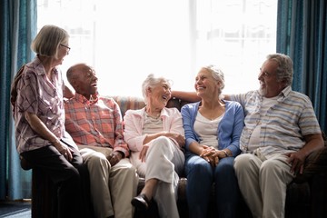 Smiling senior friends talking while sitting on couch