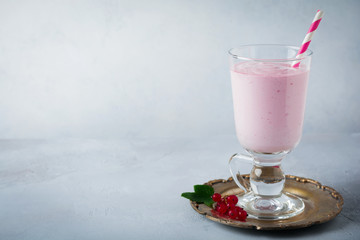Red currant yoghurt smoothies, milkshake in a glass cup on a gray concrete background. Selective focus. Copy space.