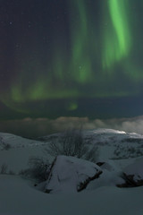 Winter, night, frozen lake and aurora borealis above the hills .