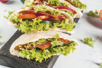 Snack. Takeaway food, street fast food. Pita bread sandwich with fresh vegetables lettuce, cucumber, tomato, radish, beef meat. On a light concrete table on a wooden tray. Copy space