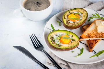 Healthy vegan breakfast. Diet. Baked avocado with egg and fresh salad from arugula, toast and butter. On a white marble plate, a light concrete table. A cup of coffee. Copy space