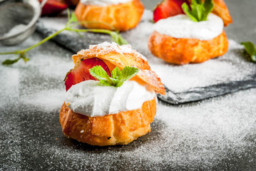 Summer desserts. Homemade baking. Cake profiteroles with whipped cream, fresh strawberries, mint and sprinkling of powdered sugar. On a black stone table. Copy space
