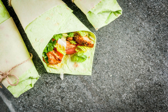 Mexican food. Healthy eating. Wrap sandwich: green lavash tortillas with spinach, fried chicken, fresh greens salad, tomatoes, yoghurt sauce. Black dark stone table. Copy space top view