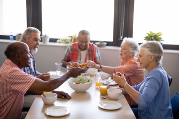 Obraz na płótnie Canvas Senior man giving food to friends sitting at table