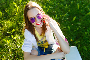 Young woman using cellphone and sitting on the grass on park at sunny day