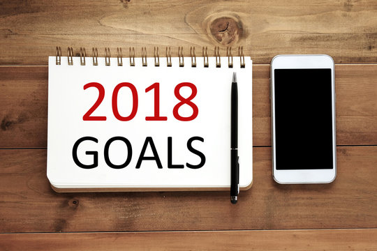 2018 goals word on notebook paper, pen and smart phone on wood background, financial concept, business strategy