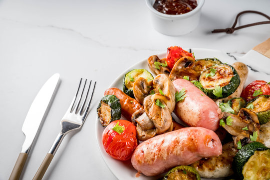 Barbecue. Assortment of various grilled meat sausages, with vegetables BBQ - mushrooms, tomatoes, zucchini, onions. On white marble table, on plate, with sauce. Copy space