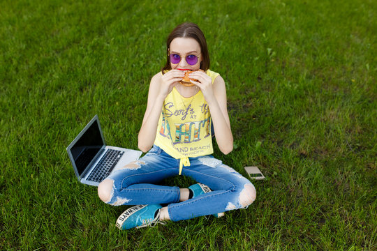 Fashion hipster style woman eating tasty hamburger on the green grass