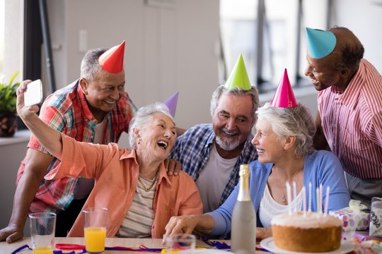 Cheerful senior woman taking selfie with friends at party
