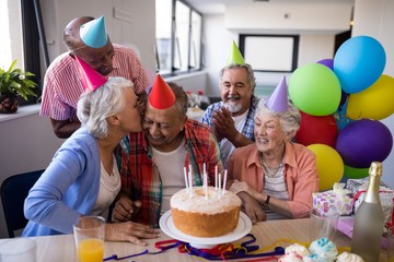 Friend kissing senior man while celebrating at party