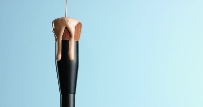 Pouring bb cream or foundation on the bristles of a professional make up brush with black handle isolated on blue
