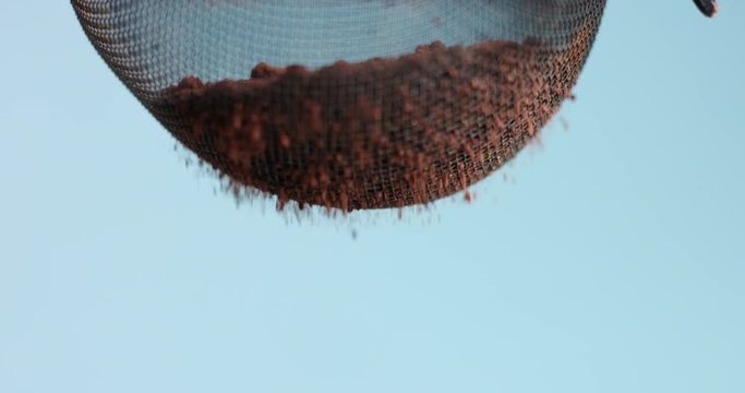 Close up shot of cocoa powder being sifted through a small handheld sift isolated on light blue