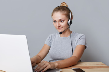 Young female operator or consulatant has headphones, looks at laptop computer, makes video calls,...