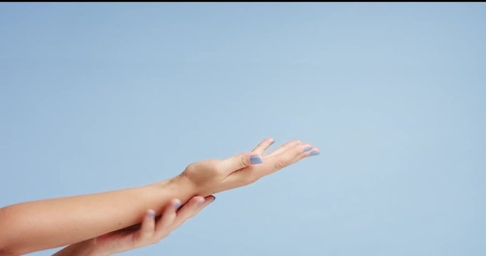 Beautiful young woman's hands with bright blue manicure, one hand gently massaging the other, isolated on light blue background