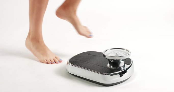 Pretty young woman's feet with blue toenails stepping on an old fashioned black an white scale with round dial isolated on white