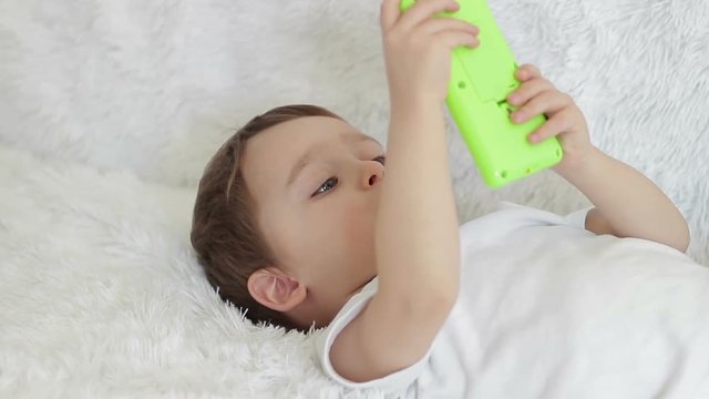 Close-up of a child lying on a couch at the back, playing with a smartphone in green